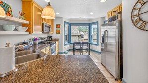 A kitchen with granite countertops, stainless steel appliances, wooden cabinets, and a dining area with a view. - Eazy Breezy: Ocean Views, Dog-Friendly Rockaway Beach Townhome for 8 (Rockaway Beach)