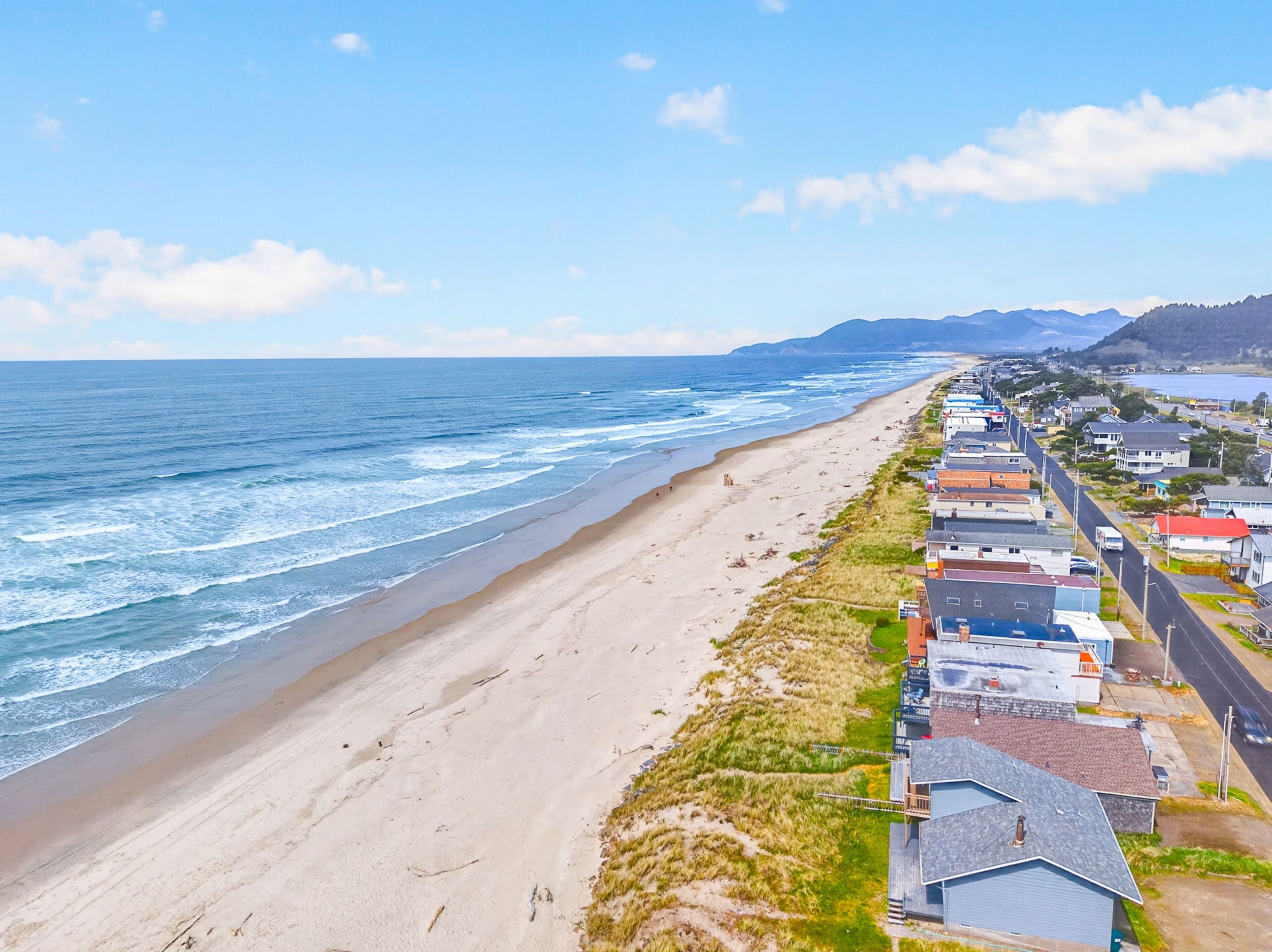 A coastal area with a beach, ocean, and a row of buildings along the shore.