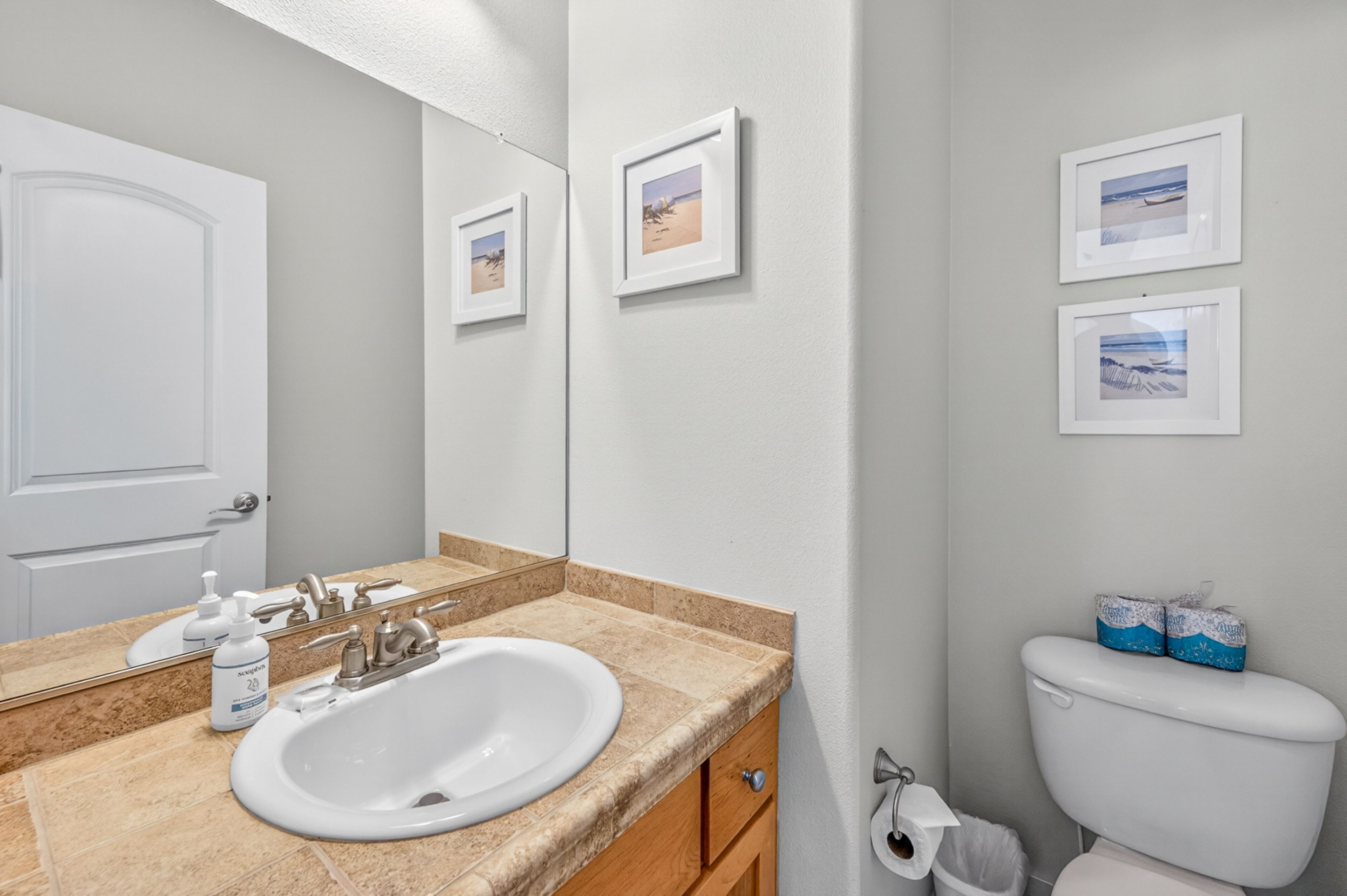 A bathroom with a sink, mirror, toilet, and framed pictures on the wall.