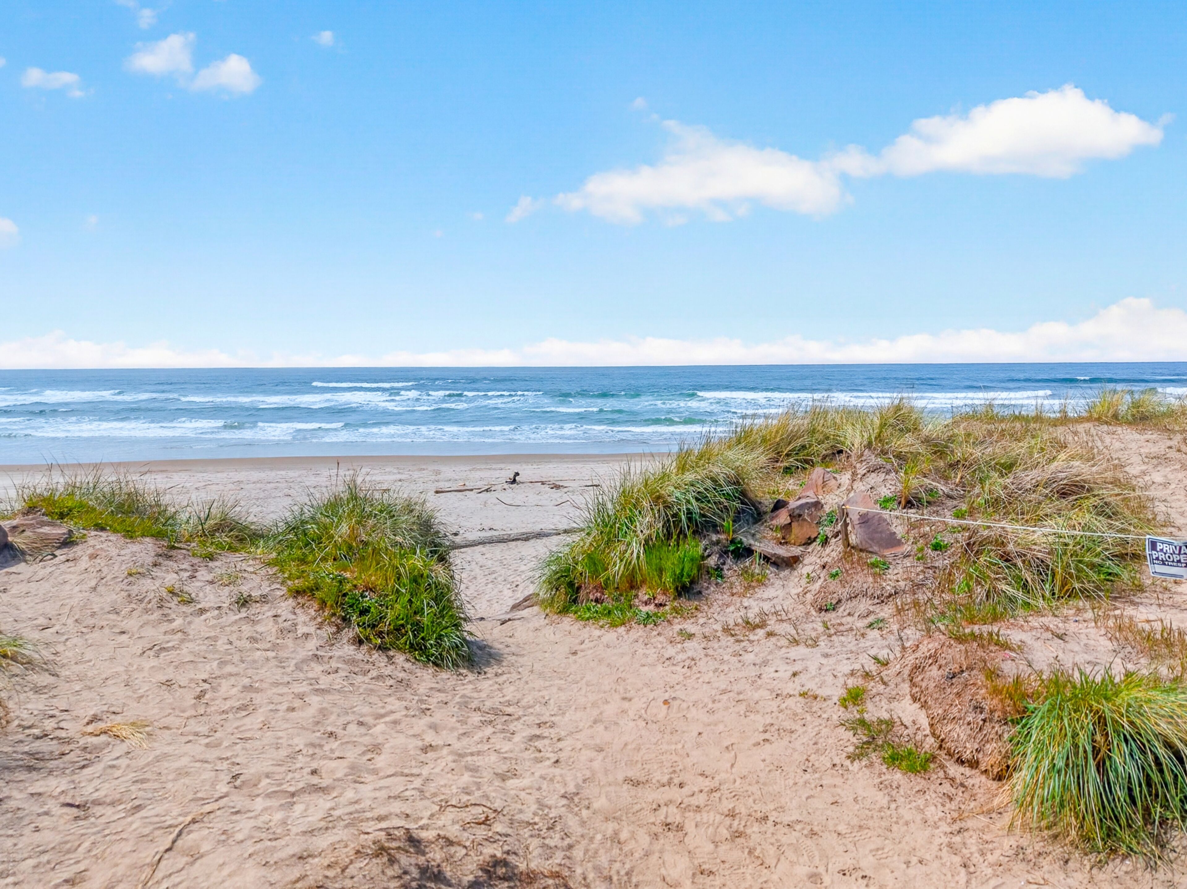 Una spiaggia sabbiosa con un cartello che indica proprietà privata, cielo sereno e l'oceano sullo sfondo.