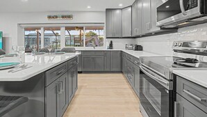 Una cucina moderna con mobili grigi, un'isola ampia con piano di lavoro bianco ed elettrodomestici in acciaio inossidabile.