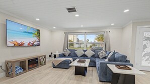 A living room with a large flat-screen TV, a sofa set, a coffee table, and a fireplace. - Canal Front Getaway | Pool, Dock, Game Room + Screened Porch (Port Richey)