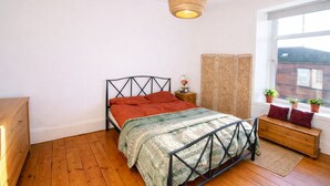 Une chambre à coucher avec un lit, une commode en bois, une fenêtre donnant sur un paysage agréable et un luminaire suspendu.
