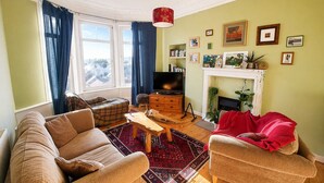Un salon comprenant un canapé, un fauteuil, un téléviseur, une cheminée et une vue sur l’extérieur.