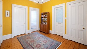 Un couloir aux murs jaunes, aux portes blanches, avec une bibliothèque en bois et un tapis à motifs.