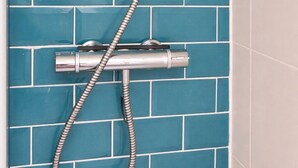 Une douche équipée d’un pommeau de douche à main et d’un flexible, le tout fixé sur un mur recouvert de carreaux bleus.