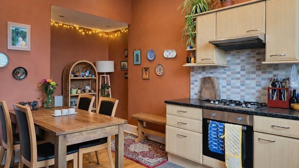 Une cuisine compacte comprenant une cuisinière, des placards et un coin repas avec des chaises et une table.