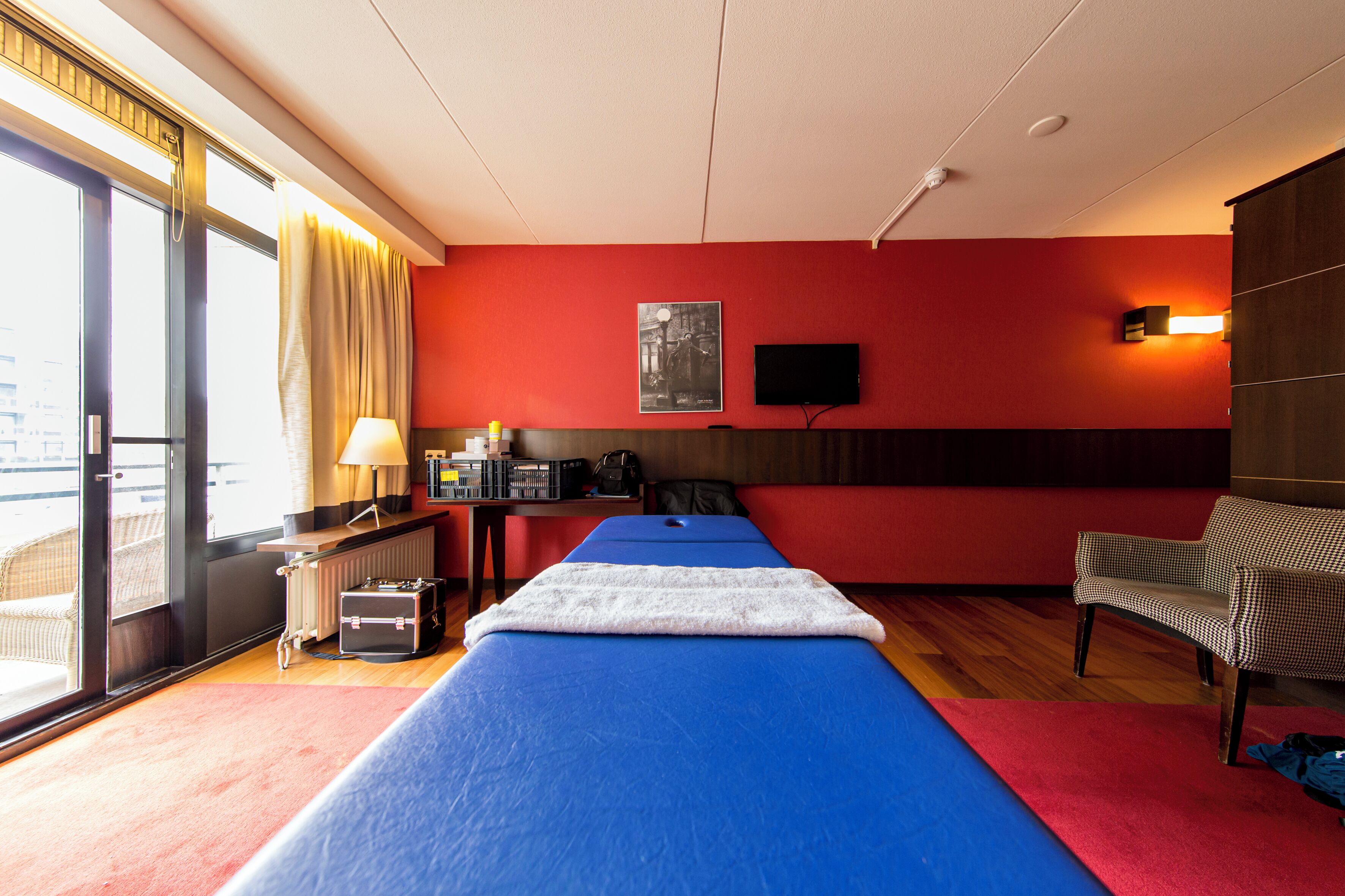 Une chambre d’hôtel équipée d’un lit, d’un bureau, d’une chaise, d’un radiateur, d’une télévision et d’une fenêtre avec des rideaux.