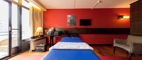 Une chambre d’hôtel équipée d’un lit, d’un bureau, d’une chaise, d’un radiateur, d’une télévision et d’une fenêtre avec des rideaux.