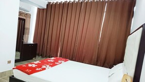 Une chambre à coucher avec un lit, une tête de lit en bois, une couvre-lit à motifs floraux rouges et des rideaux marron.