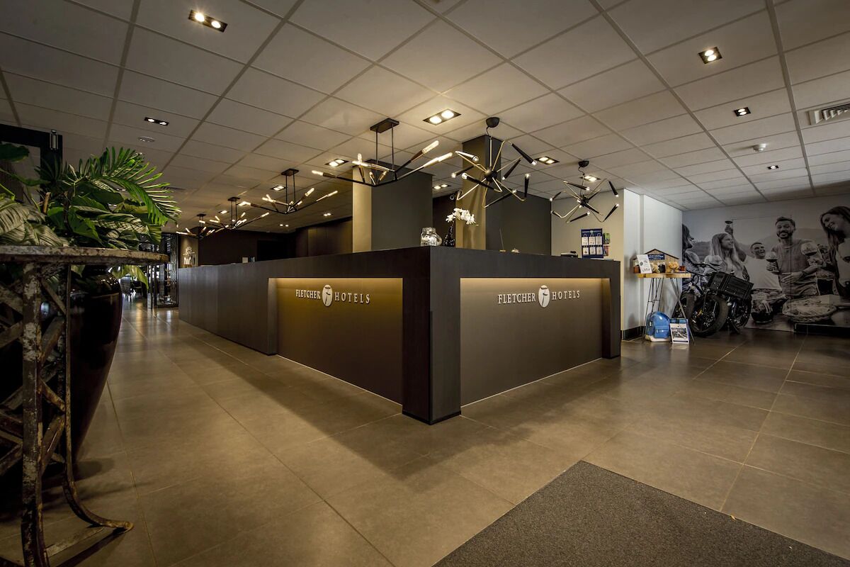 Ein Empfangstresen mit 'Fletcher Hotels' Schriftzug, ein Fliesenboden und eine Decke mit eingelassenen Leuchten.