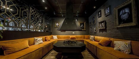 A modern lounge with a central coffee table, orange sofas, and framed pictures on the walls.