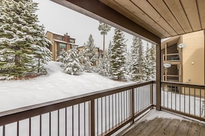 A wooden deck with a railing, snow-covered ground, and buildings in the background. - New to Market! Ski in/Ski Out Big Sky Resort (Big Sky)