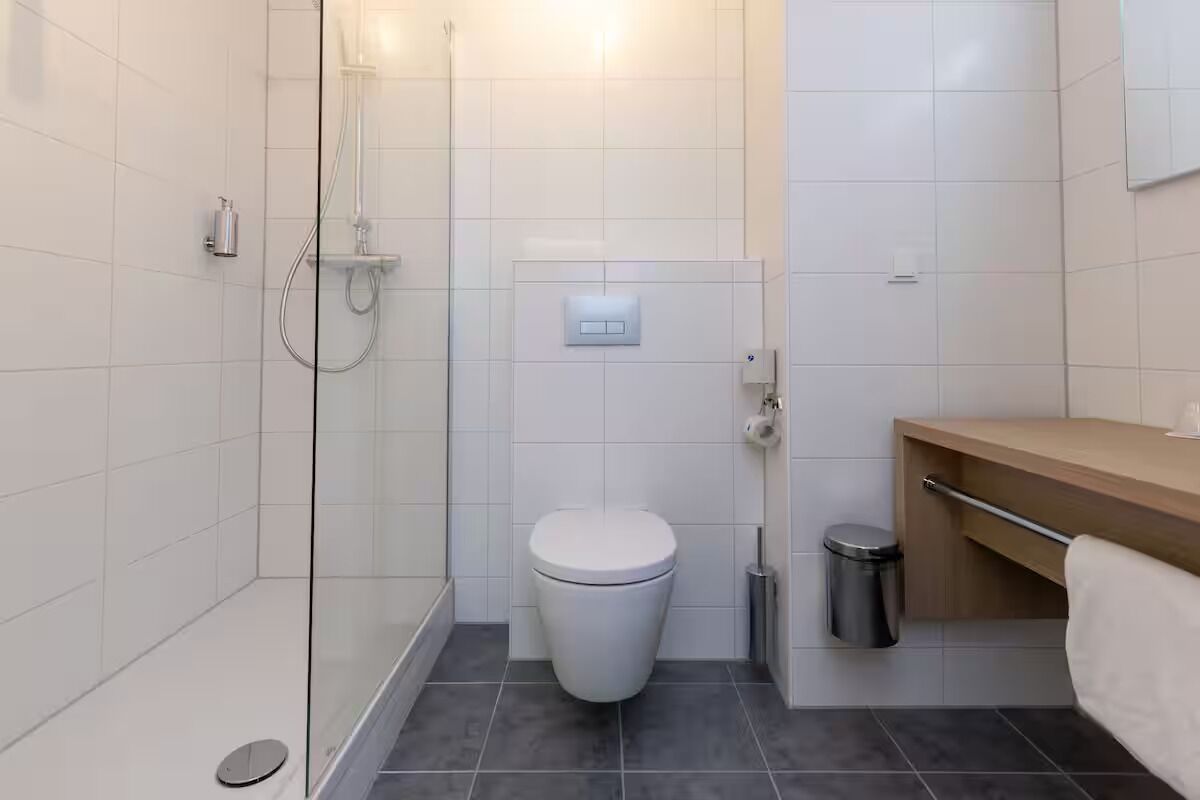 Ein modernes Badezimmer mit Duschkabine aus Glas, einer weißen Toilette und einem hölzernen Waschtisch mit Handtuchhalter.