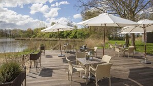 An outdoor patio with wicker furniture, white umbrellas, and a view of a lake. - Perfect for Relaxation: Scenic Views and Dining in a Beautiful Setting (Velsen-Zuid)