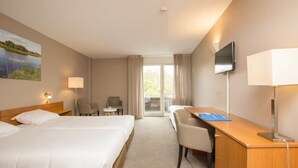 Hotellihuone, jossa on kaksi sänkyä, työpöytä, tuoli, televisio, lamppu ja taulu seinällä.