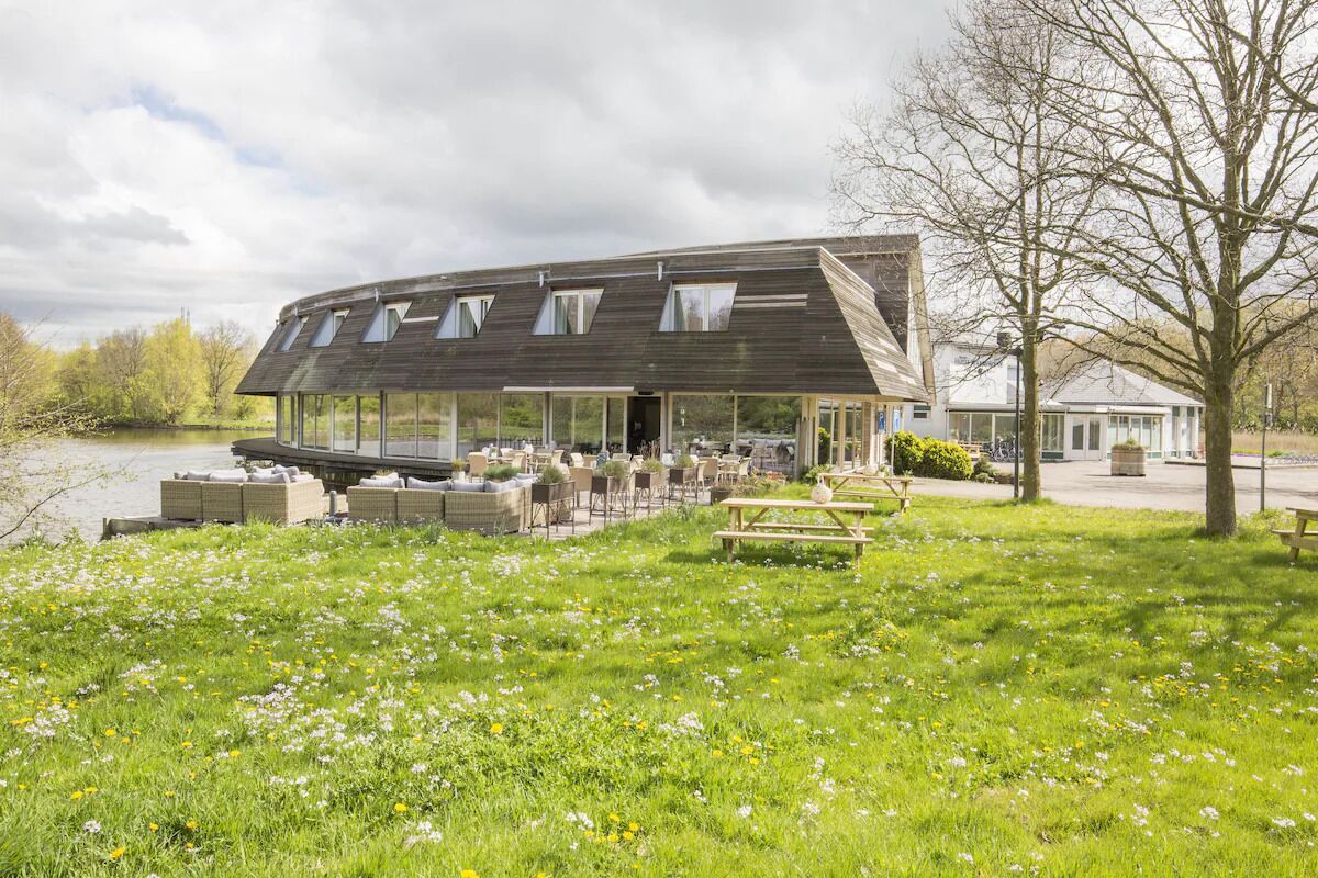 A modern building with a curved roof, large windows, and outdoor seating.