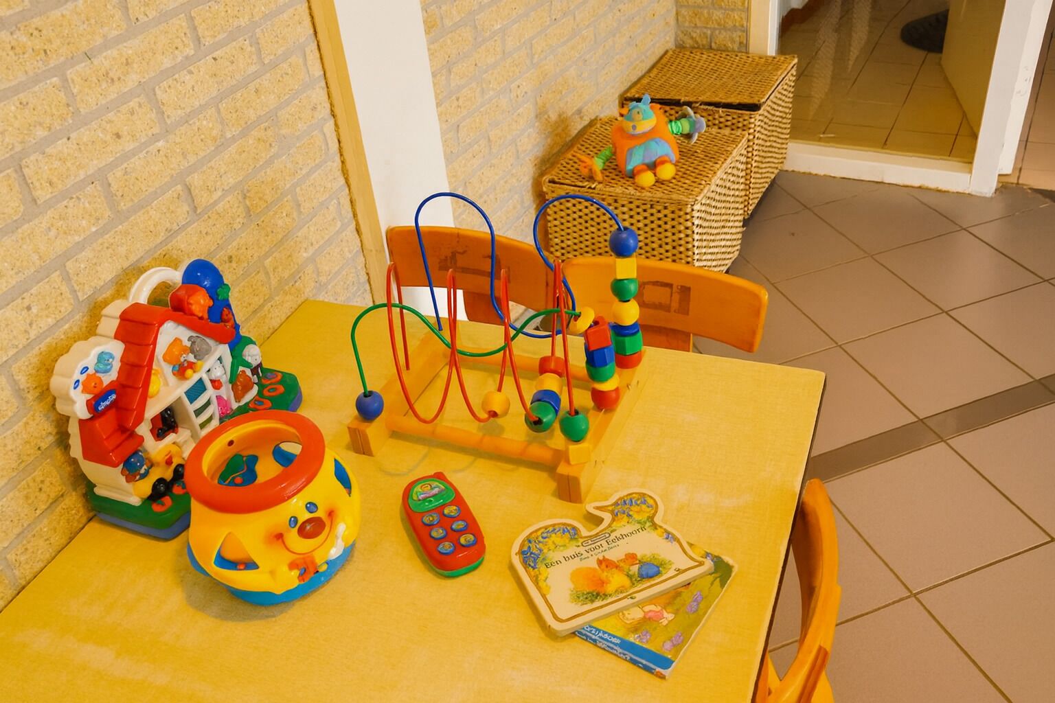A yellow table with a toy abacus, a toy house, a toy car, and a book.