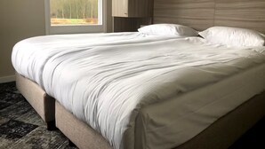 Una cama bien hecha con cabecera, una ventana con vistas a árboles y una alfombra estampada.