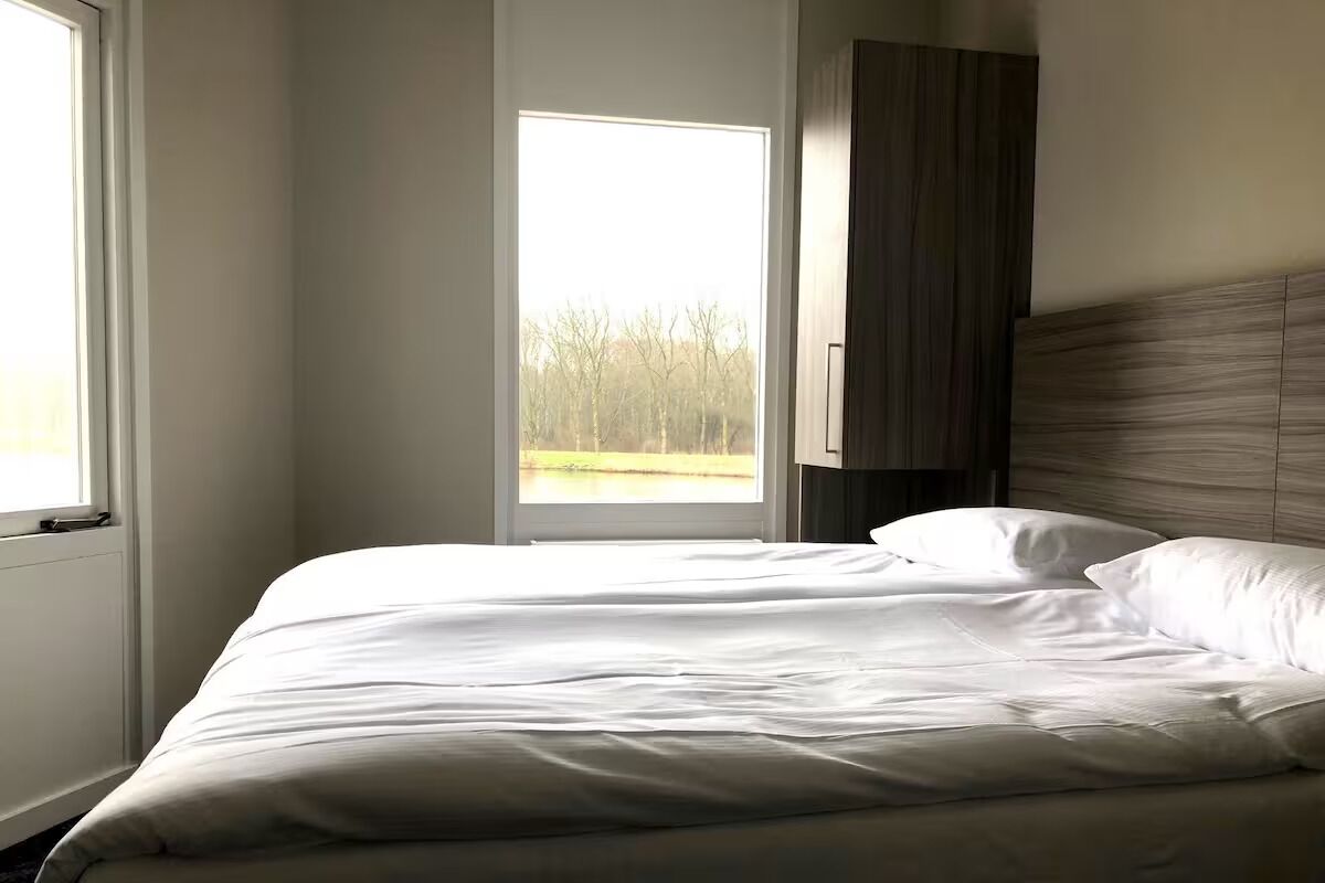 Een slaapkamer met een groot raam, een bed en een houten hoofdbord.