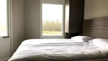 Een slaapkamer met een groot raam, een bed en een houten hoofdbord.