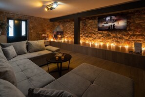 A modern living room with a stone wall, a fireplace, a sofa, a coffee table, and a TV mounted on the wall. - Villa Green Escape: Your Serene Family Getaway Awaits (Grubine)