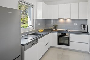 A modern kitchen with white cabinets, a stainless steel refrigerator, a built-in oven, and a coffee machine. - Villa Green Escape: Your Serene Family Getaway Awaits (Grubine)