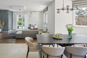 A modern dining area with a dark table, four chairs, a vase with flowers, and a bowl of fruit. - Villa Green Escape: Your Serene Family Getaway Awaits (Grubine)