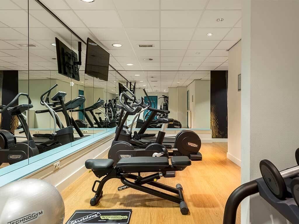 Un gimnasio con máquinas de cardio, bancos de pesas y espejos.