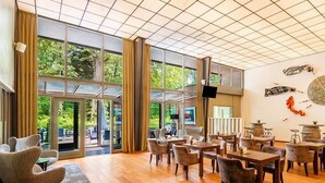 A spacious indoor area with large windows, wooden flooring, and multiple seating arrangements.