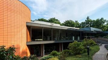 A modern building with a curved brick facade, large glass windows, and a pathway leading to a bench area.
