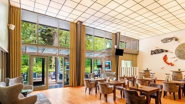 Un amplio espacio interior con ventanas grandes, suelo de madera y varios conjuntos de asientos.