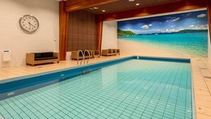 An indoor swimming pool with a tiled floor, wooden ceiling, and a wall clock.