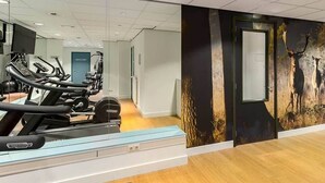 A gym with exercise equipment, a mirror, and a wall with a nature-themed mural.