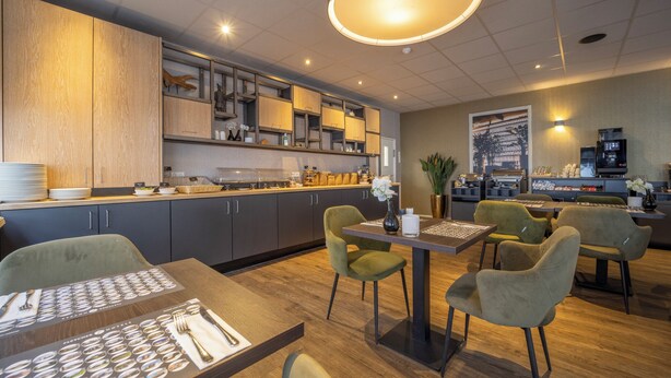 Un restaurant moderne avec un comptoir en bois, des chaises vertes et un grand luminaire suspendu.