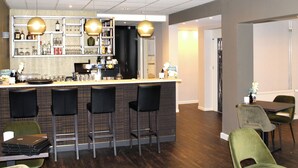 Un espace bar avec des tabourets, un comptoir avec des bouteilles, des verres et une machine à café. Des chaises et une table se trouvent dans la salle à manger adjacente.