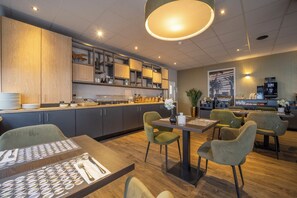 Een modern restaurant met een houten toonbank, groene stoelen en een grote hanglamp.