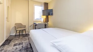 Een hotelkamer met een bed, bureau, stoel, televisie en raam.