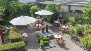 Een terras buiten met tafels, stoelen, parasols en een geplaveid pad van baksteen.