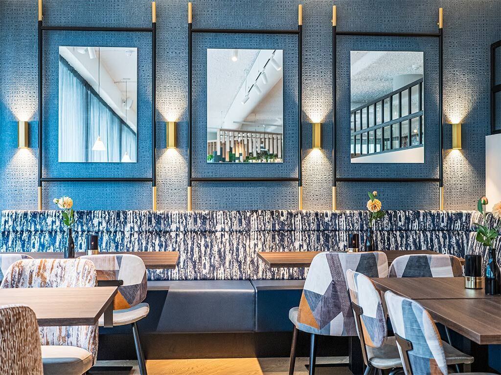 A modern restaurant interior with a blue textured wall, framed windows, and contemporary furniture.