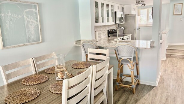 Uma sala de jantar com mesa de madeira, jogos americanos trançados e cadeiras de vime.