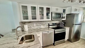 Uma cozinha moderna com armários brancos, geladeira de aço inoxidável, micro-ondas, forno e lava-louças.