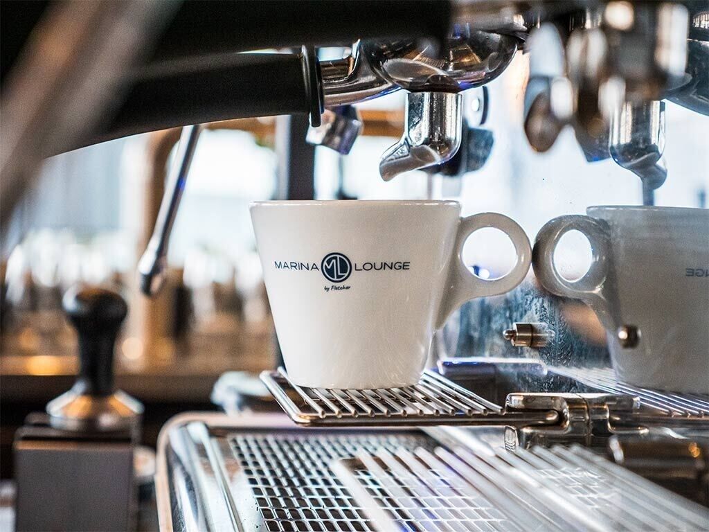 A coffee machine with a cup labeled 'MARINA LOUNGE' and a second cup.