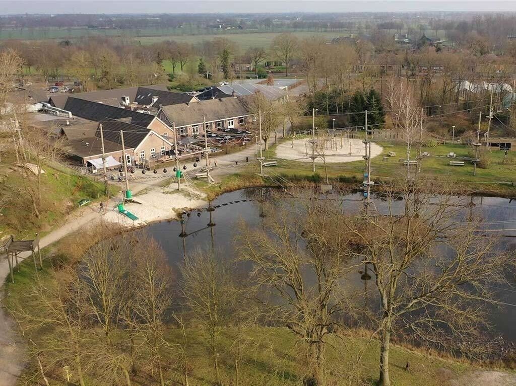 An aerial view of a building with a large parking area, a pond, and surrounding greenery.
