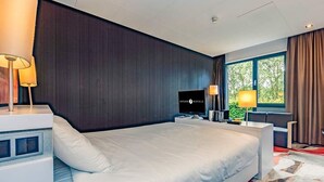 Habitación de hotel con una cama grande, televisor, escritorio con lámpara y ventana con cortinas.
