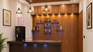 Ein Hotel-Empfangsbereich mit Marmorboden, einer Rezeption, einer Kaffeemaschine, einem Wasserspender und einem an der Wand befestigten Spirituenschrank.