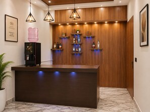 Een hotel receptie met een marmeren vloer, een receptiebalie, een koffieapparaat, een waterdispenser en een wandplank voor drankflessen.