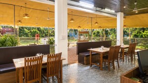 Ein Restaurant im Freien mit Holztischen und -stühlen, einer Sitzgelegenheit und Blick ins Grüne.