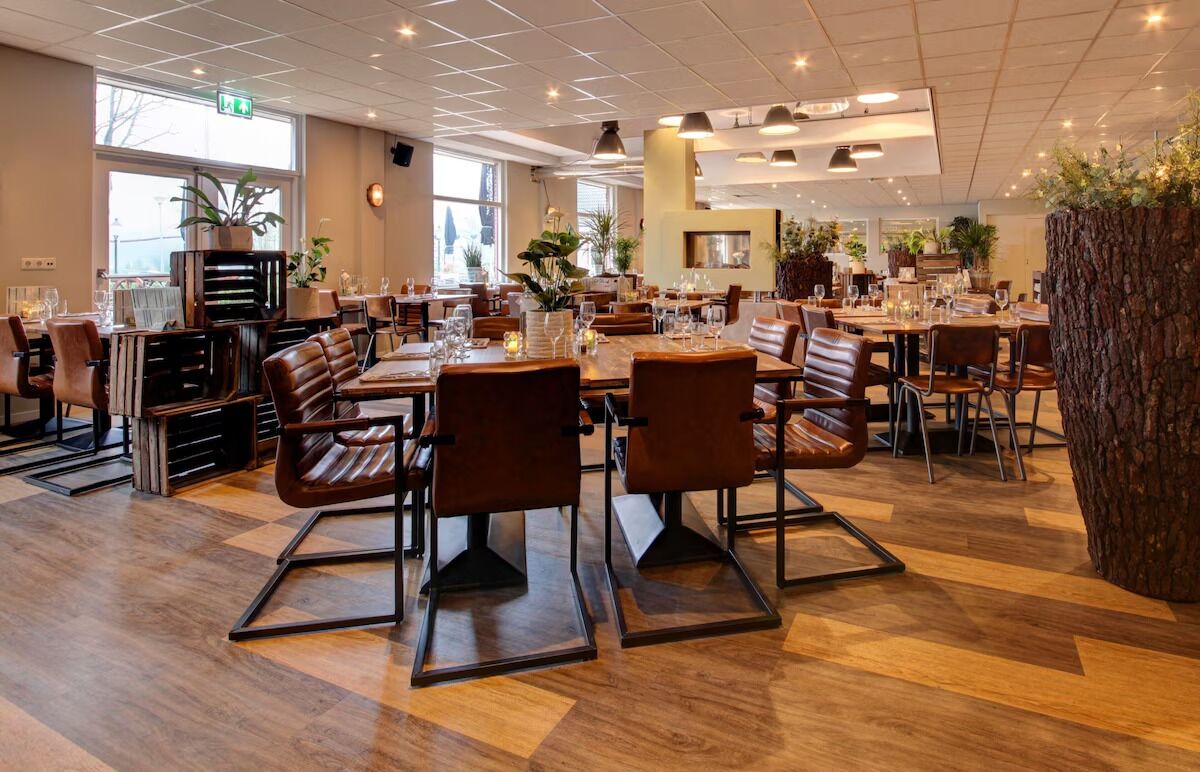 A restaurant with wooden flooring, leather chairs, and tables set for dining.