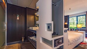 Ein modernes Hotelzimmer mit Bett, Schreibtisch, Badezimmer und Blick auf Grünflächen.